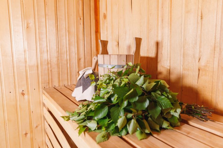 Traditioneller Birken-Saunabesen liegt auf einer Holzbank in einer finnischen Sauna für Garten