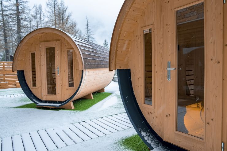 Zwei hochwertige Gartensaunas aus Holz im Fassdesign im Winter – moderne Außensauna für den Garten mit Glasfront und natürlicher Holzoptik
