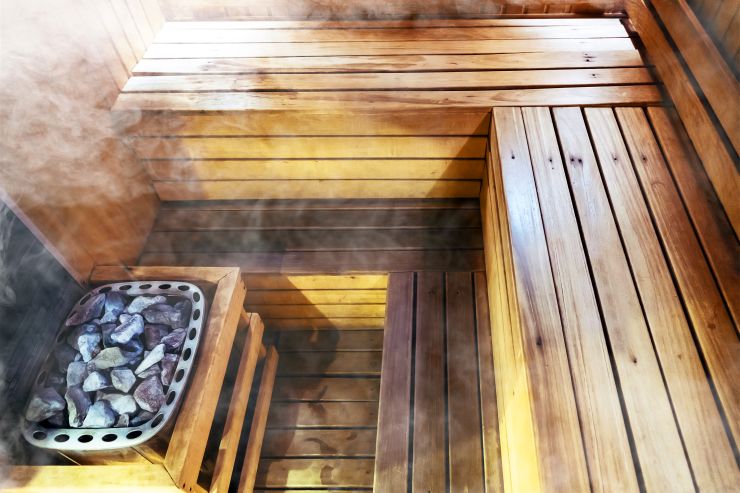 Innenansicht einer modernen finnischen Sauna mit Holzliegen, Saunaofen mit heißen Steinen und aufsteigendem Dampf – klassische Gartensauna aus Holz