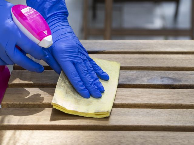 Reinigung Gartenmöbel Holz mit Reinigungsspray und Schwamm – behandschuhte Hand säubert Holzlatten