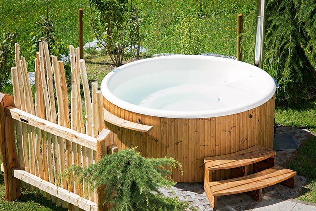 Holzverkleideter Außenwhirlpool im Garten mit Treppe und natürlichem Holzsichtschutz, eingebettet in eine grüne Landschaft