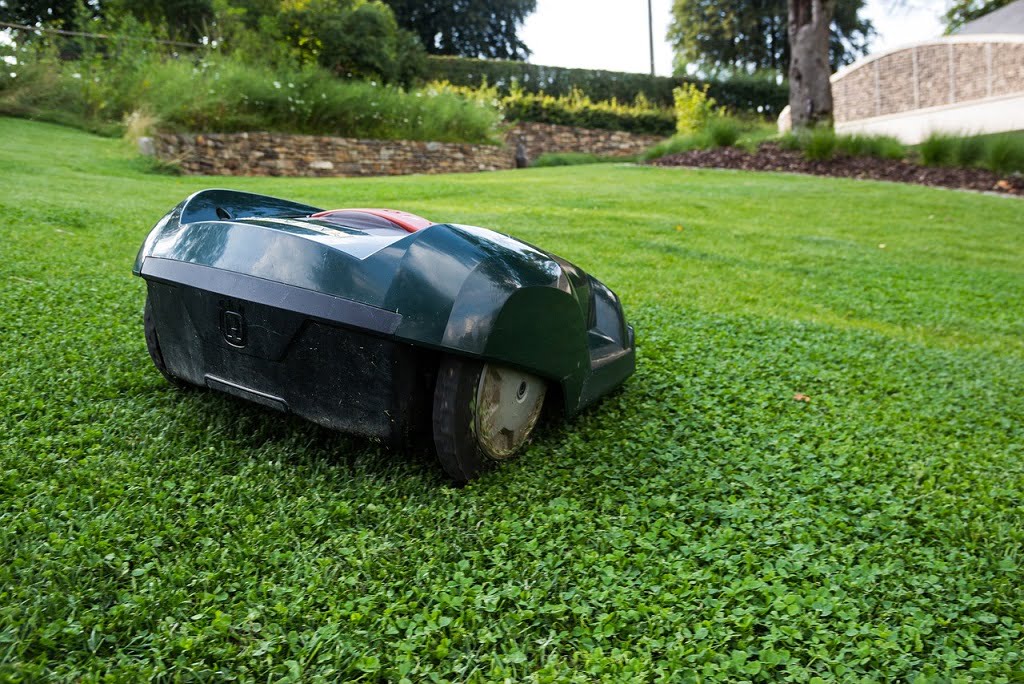 Autonomer Rasenmäher Roboter arbeitet selbstständig auf einem gleichmäßig geschnittenen, satten Gartenrasen - gepflegter Privatgarten mit Grünfläche und Landschaftselementen im Hintergrund
