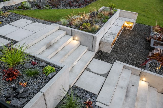 Moderne Gartentreppe aus Sichtbeton mit integrierter Beleuchtung, Betonstufen und Hochbeeten – zeitgemäße Gartengestaltung mit Beton für Garten, Kies und Zierpflanzen