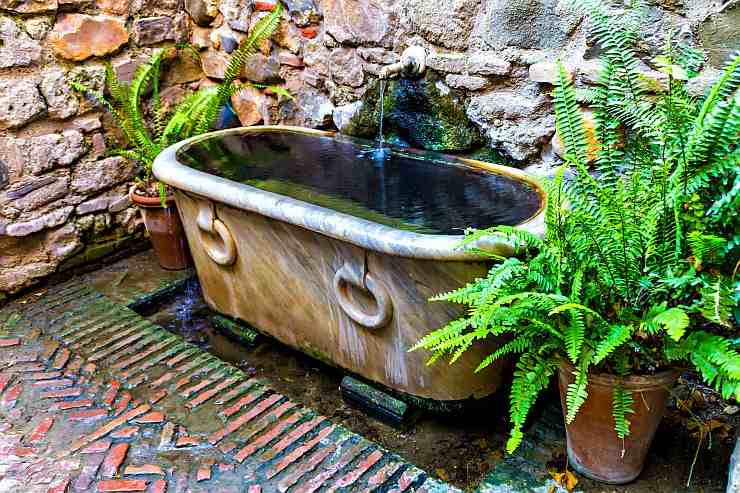 Alte Badewanne als Regenwasserspeicher im Garten, fließendes Wasser aus dem Wasserhahn