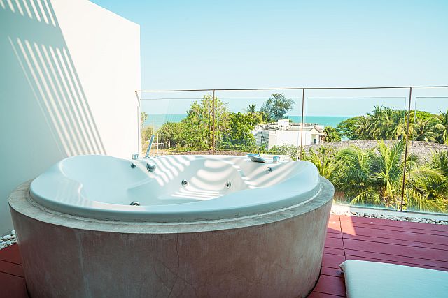 Whirlpool auf einer Terrasse mit Glasgeländer und Meerblick, moderner Jacuzzi für Wellness und Entspannung im Freien, umgeben von Palmen und tropischer Landschaft
