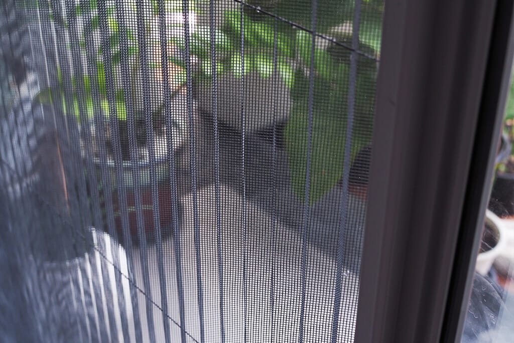 Feines schwarzes Moskitonetz an einer geöffneten Balkon- oder Terrassentür, das zuverlässig vor Mücken und Insekten schützt, während der Blick ins Grüne und die Luftzirkulation erhalten bleiben
