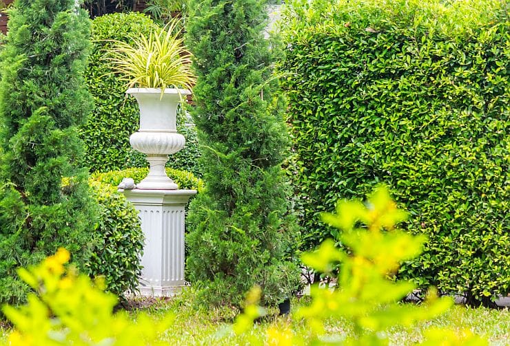 Säulen für den Garten als ein Blickfänger in einem grünen Garten mit Tannenbäumen und Sträuchern 